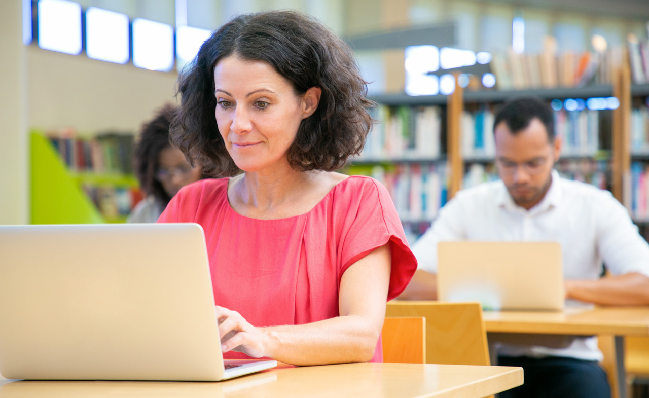 Mujer mayor que trabaja con la computadora portátil en una biblioteca.